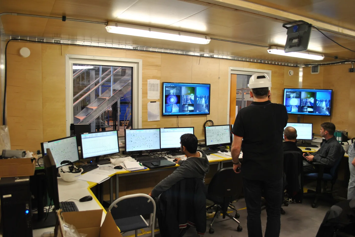 Imagen ilustrativa: equipo técnico supervisa pruebas de aceptación de equipos de proceso desde una sala de control con pantallas operativas.